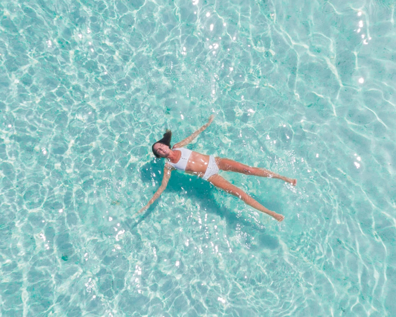 A woman in a white swimsuit floats in clear blue water
